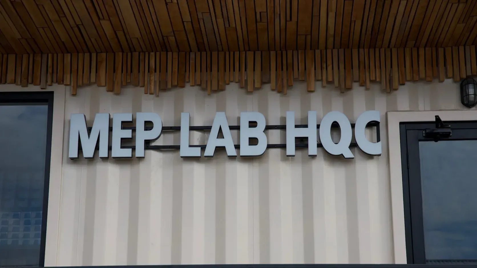 The MEP LAB HQC sign on the façade of the in-house engineering laboratory, under a ceiling of timber slats