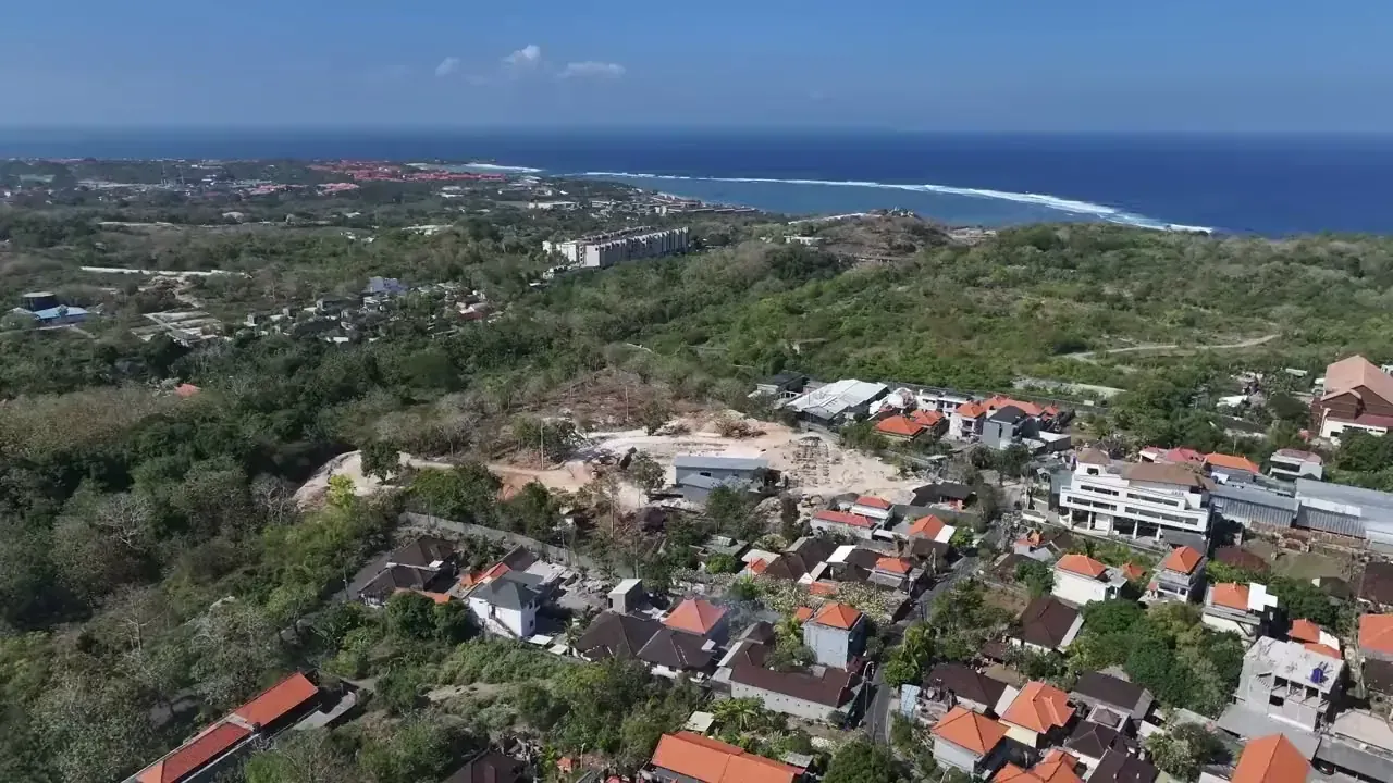 Aerial view over the Bukit Peninsula in south Bali: red-roofed houses and green hillside running down to the Indian Ocean, with surf along the reef