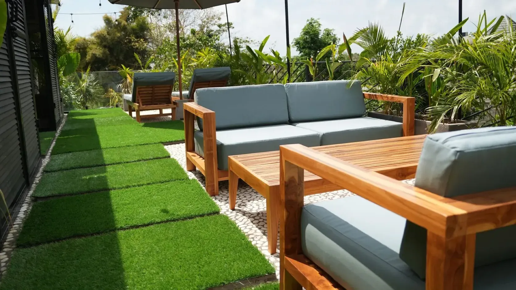 Rooftop lounge of a Black Rock villa in Ungasan: teak sofas beside a strip of lawn, sun loungers and a parasol among palms