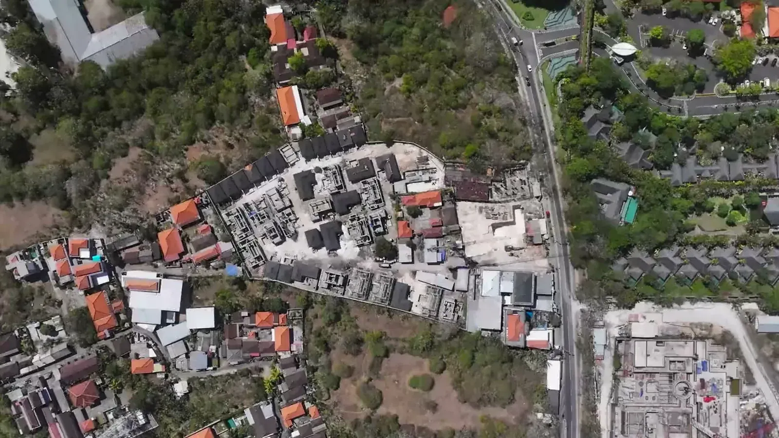 Satori in Sawangan, Nusa Dua, from directly above: villas under construction among red-roofed houses, beside the coast road and the resort grounds across it