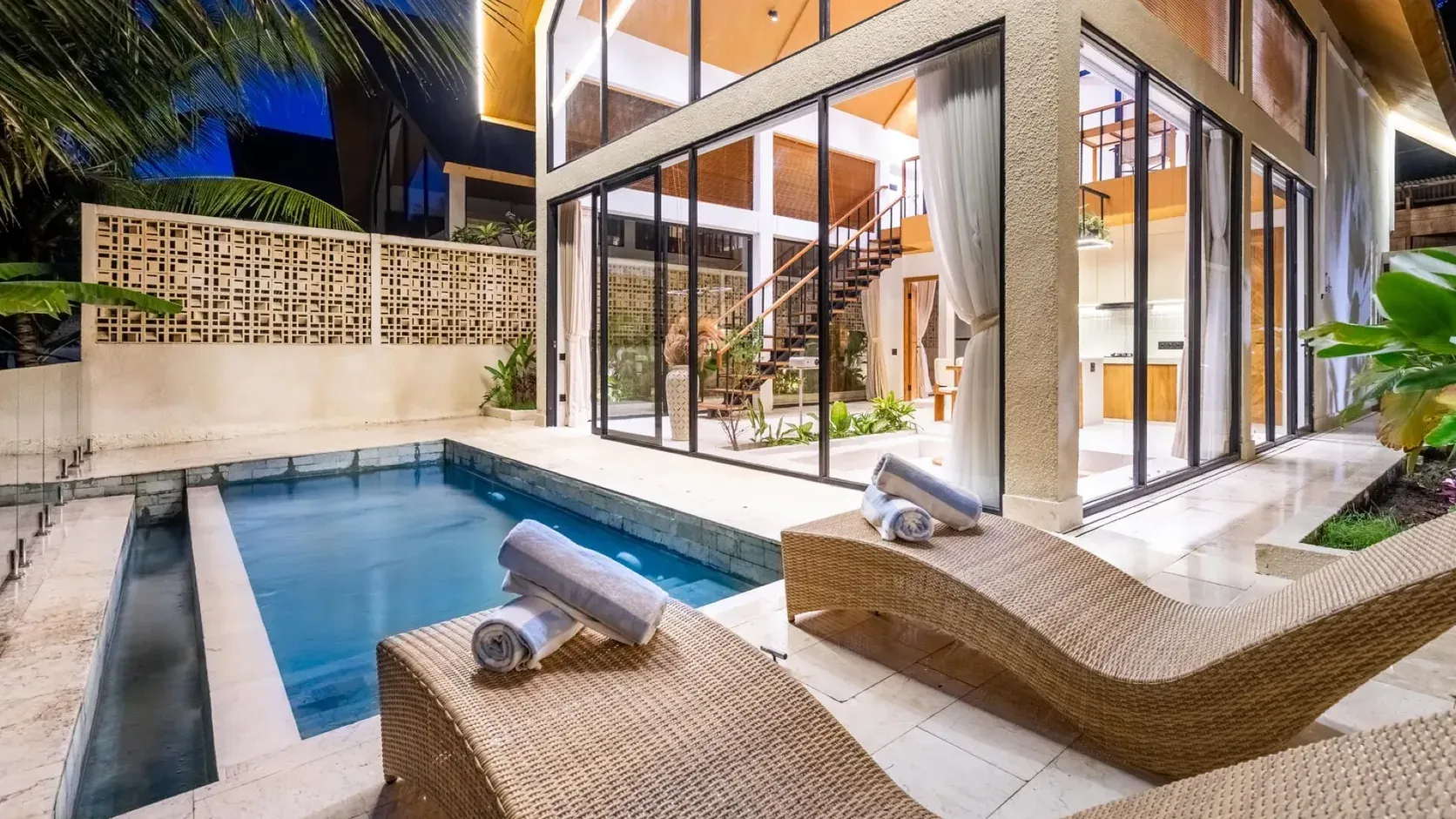 A Dzen Green Fields villa near Ubud at twilight: plunge pool, rattan loungers and a double-height glass living room